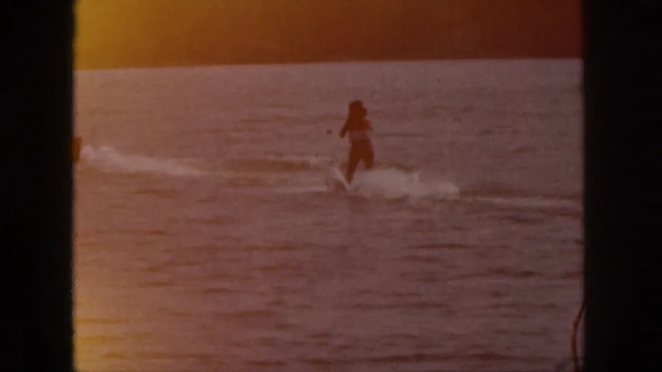 1961 Michigan 8mm home-movie frame showing a distant person riding a personal watercraft across a lake in warm light.
