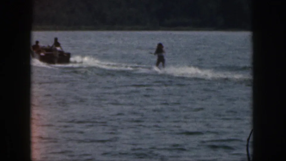 A small motorboat with passengers pulls a water skier across a Michigan lake in 1961 home-movie footage.