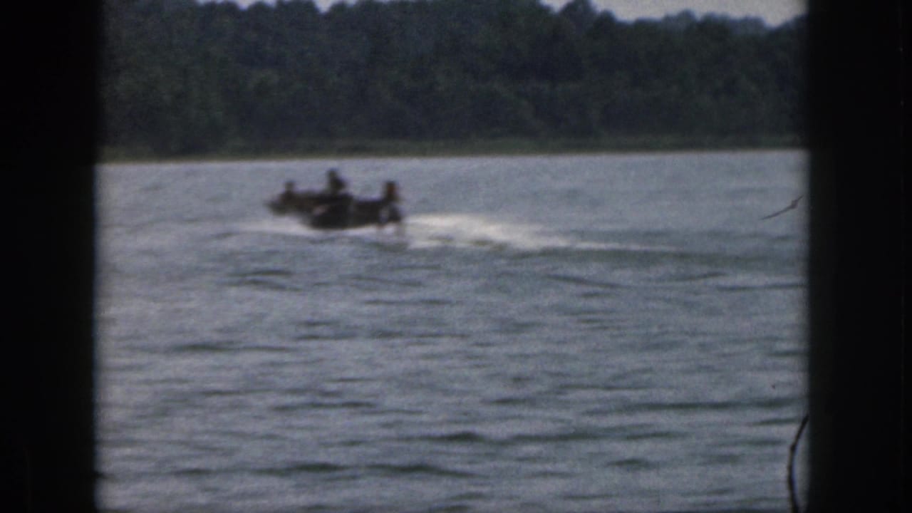 1961 Michigan 8mm frame showing a small motorboat moving across open lake water near a tree-lined shore.