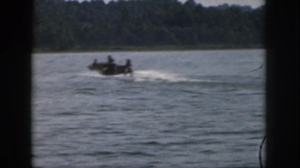 1961 Michigan 8mm frame showing a small motorboat moving across open lake water near a tree-lined shore.