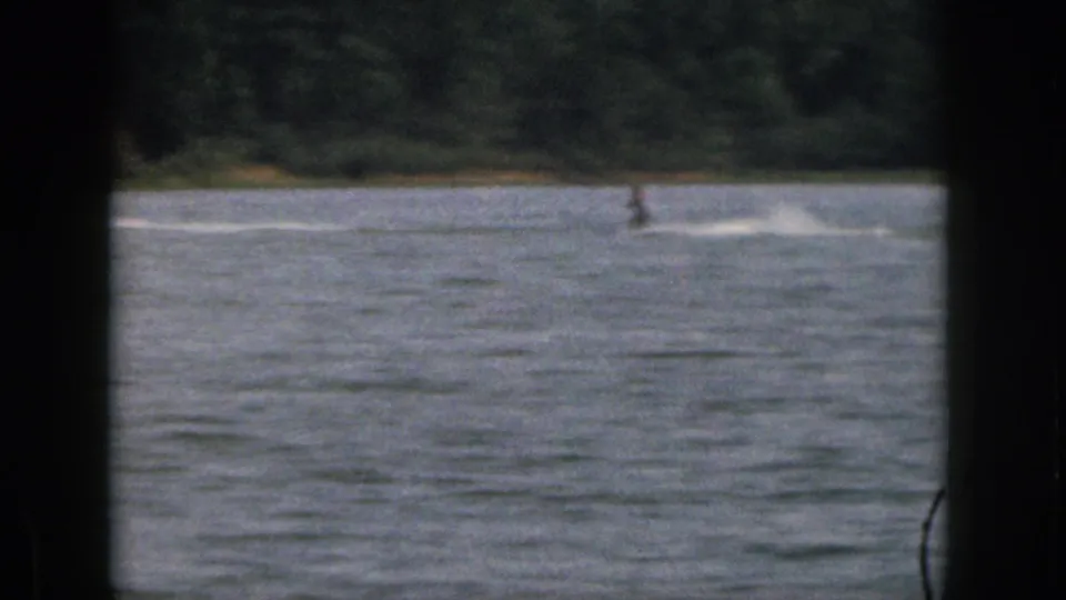 Soft 8mm frame of a distant water skier on a Michigan lake, with wake lines crossing the water.