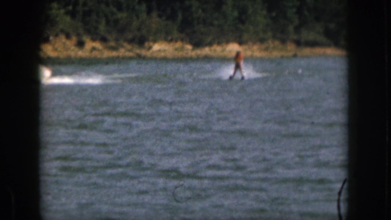 1961 Michigan 8mm frame showing a distant water skier in an orange life jacket crossing a lake behind an unseen motorboat.