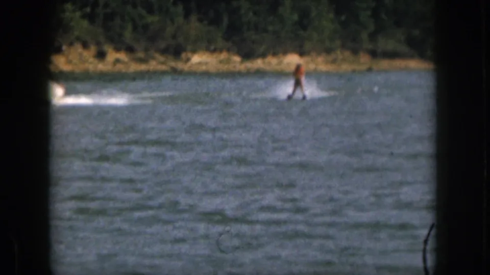 1961 Michigan 8mm frame showing a distant water skier in an orange life jacket crossing a lake behind an unseen motorboat.