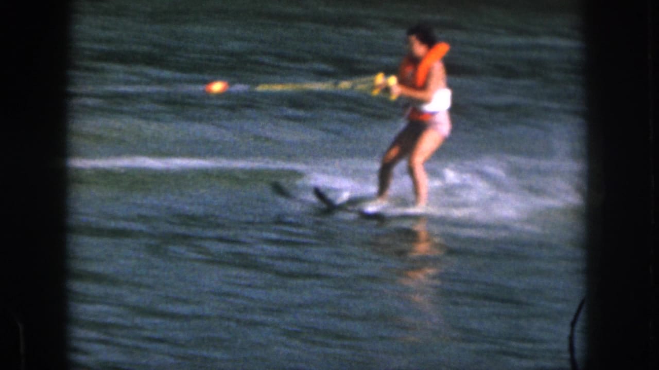 1961 Michigan 8mm frame showing a water skier in an orange life vest holding a yellow tow rope on a lake.