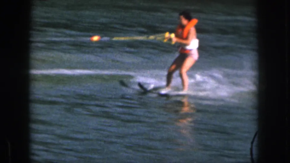1961 Michigan 8mm frame showing a water skier in an orange life vest holding a yellow tow rope on a lake.