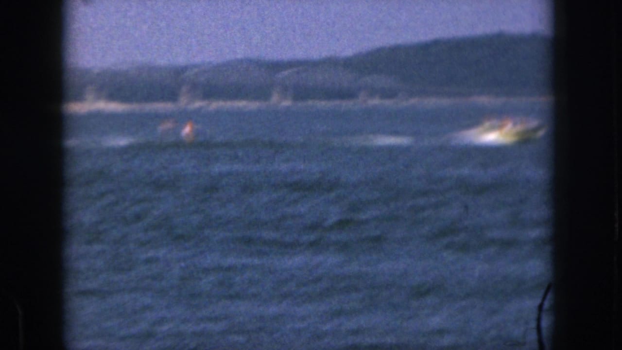 Distant motorboat and skier move across open lake water with wooded hills beyond.