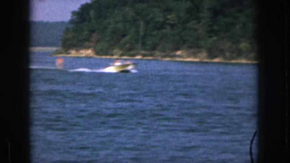 1961 Michigan 8mm frame showing a motorboat and trailing water skier moving across a wooded lake scene.