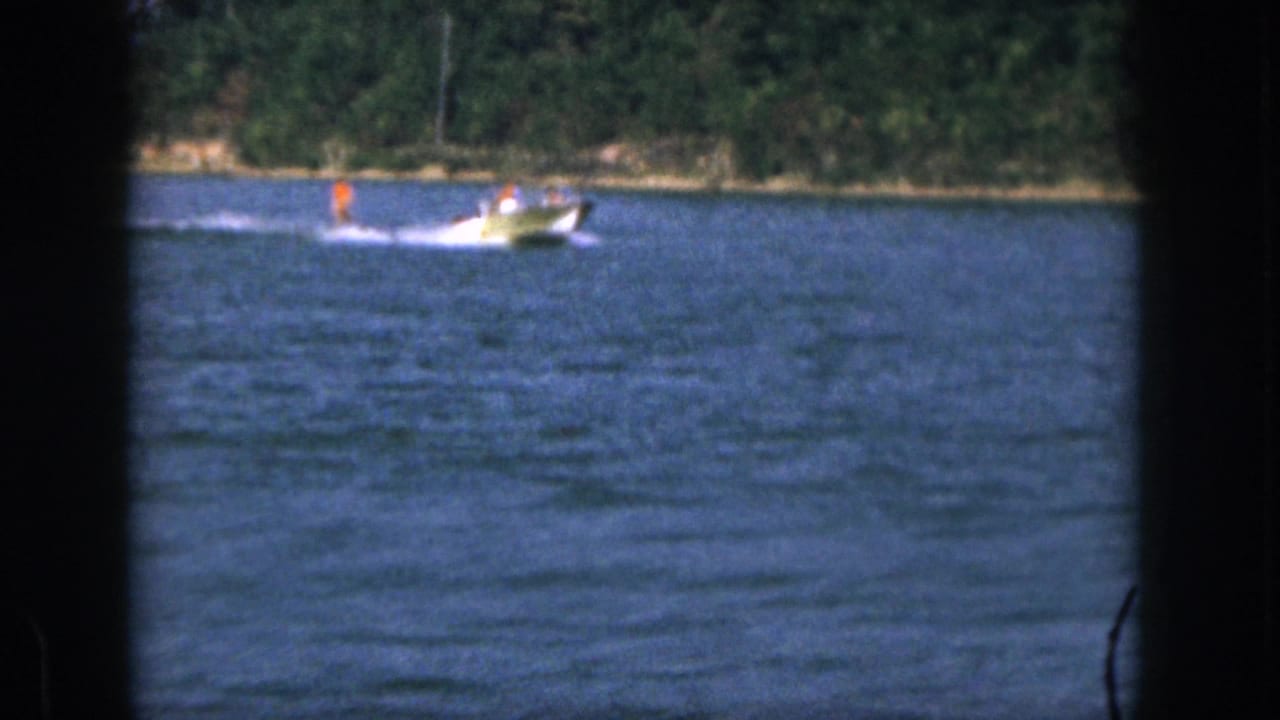 1961 Michigan 8mm frame showing a small motorboat speeding across blue lake water near a tree-lined shore.