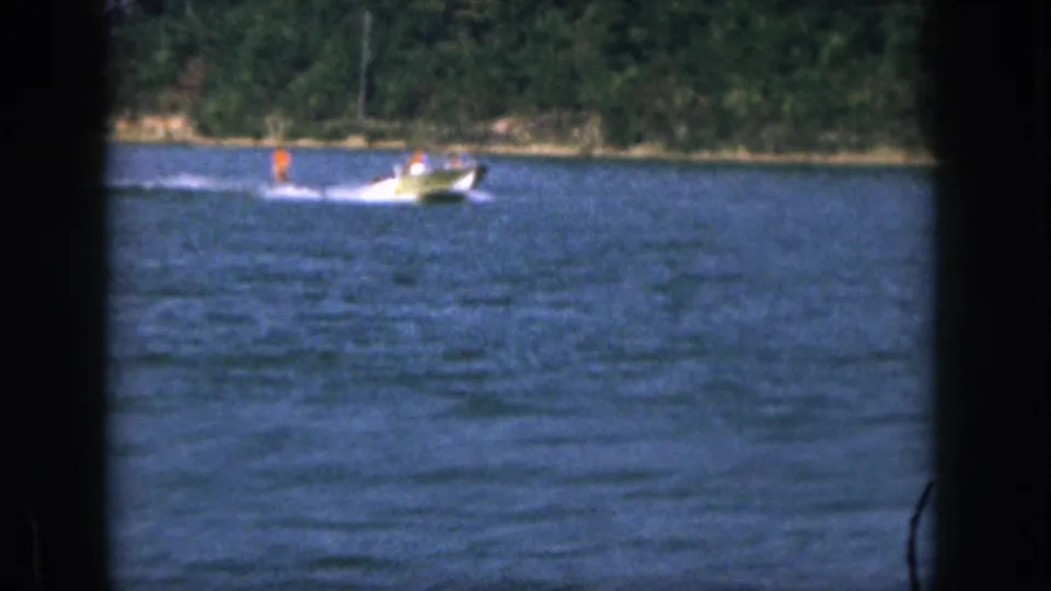 1961 Michigan 8mm frame showing a small motorboat speeding across blue lake water near a tree-lined shore.