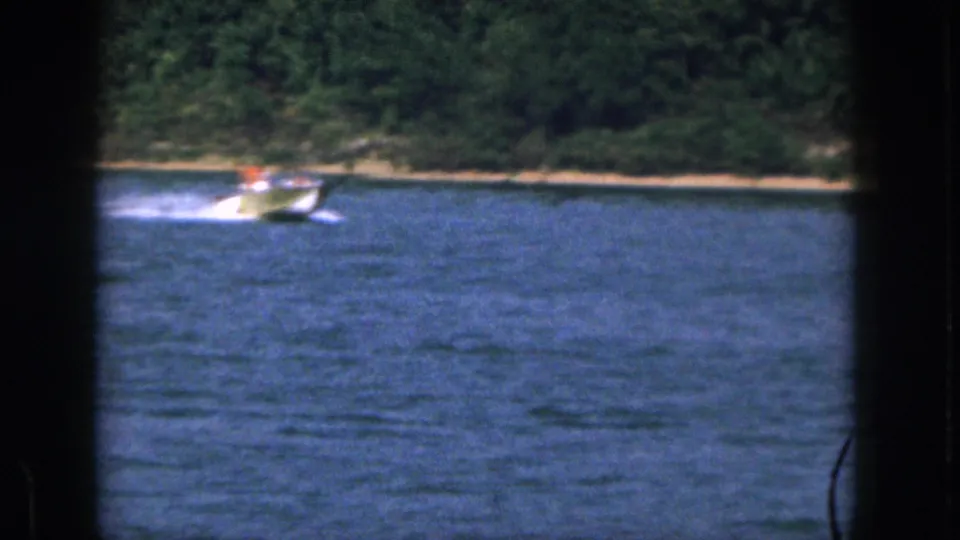 1961 Michigan 8mm still of a small motorboat moving across a lake with a wooded shore in the background.