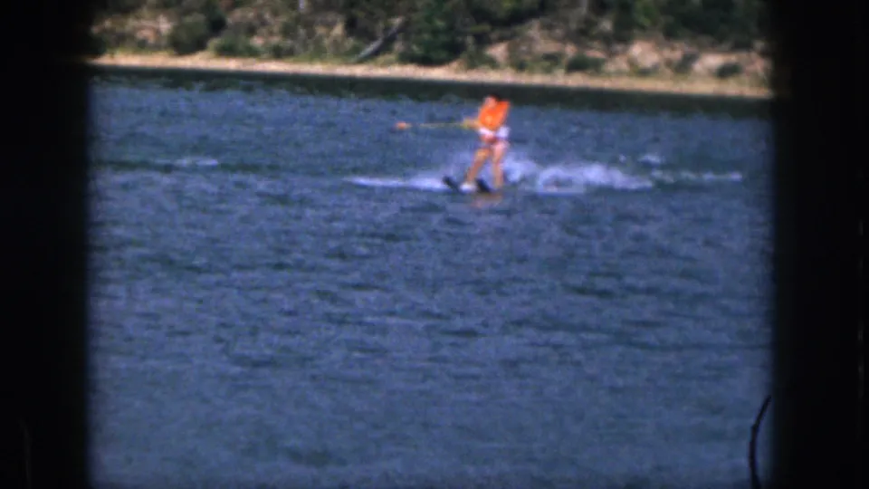 1961 Michigan 8mm frame showing a skier in an orange life vest holding a tow rope on a calm pond.