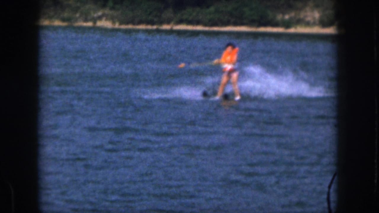 In supplied 1961 Michigan home-movie footage, a woman in an orange life vest skis across a lake while holding a tow rope.