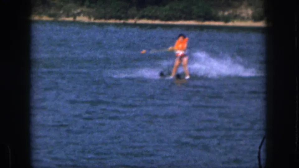 In supplied 1961 Michigan home-movie footage, a woman in an orange life vest skis across a lake while holding a tow rope.