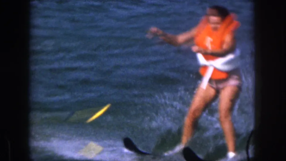 The woman appears to lose balance on water skis during the lake outing, with one ski lifting and water spray around her.