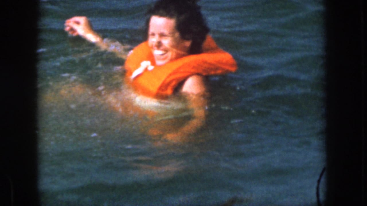 Woman in an orange life vest laughing and splashing in lake water.