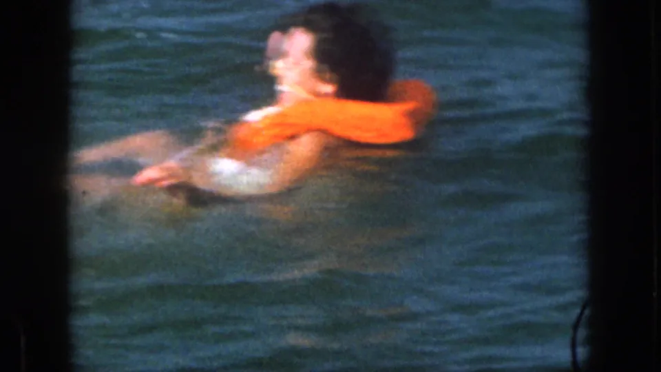 A side view shows the woman turning in the lake while the orange life vest stays prominent in the 8mm frame.