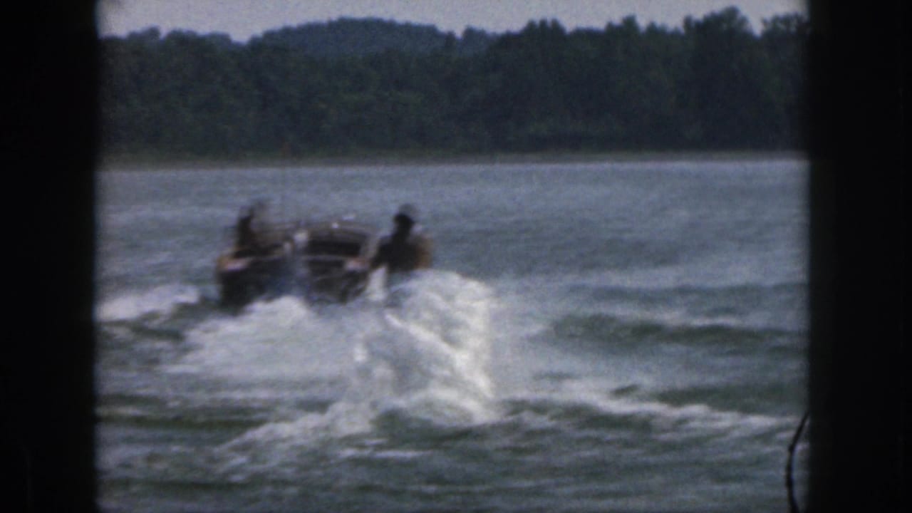 A skier trails a motorboat through choppy lake water near a distant tree line.