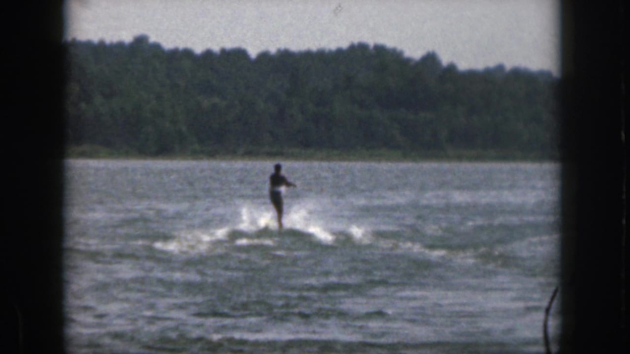 Distant water skier glides over the lake with a low wake behind them.