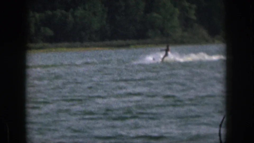 Near the end of the Michigan lake shot, the skier leans at a distance while spray and wake stretch across the water.