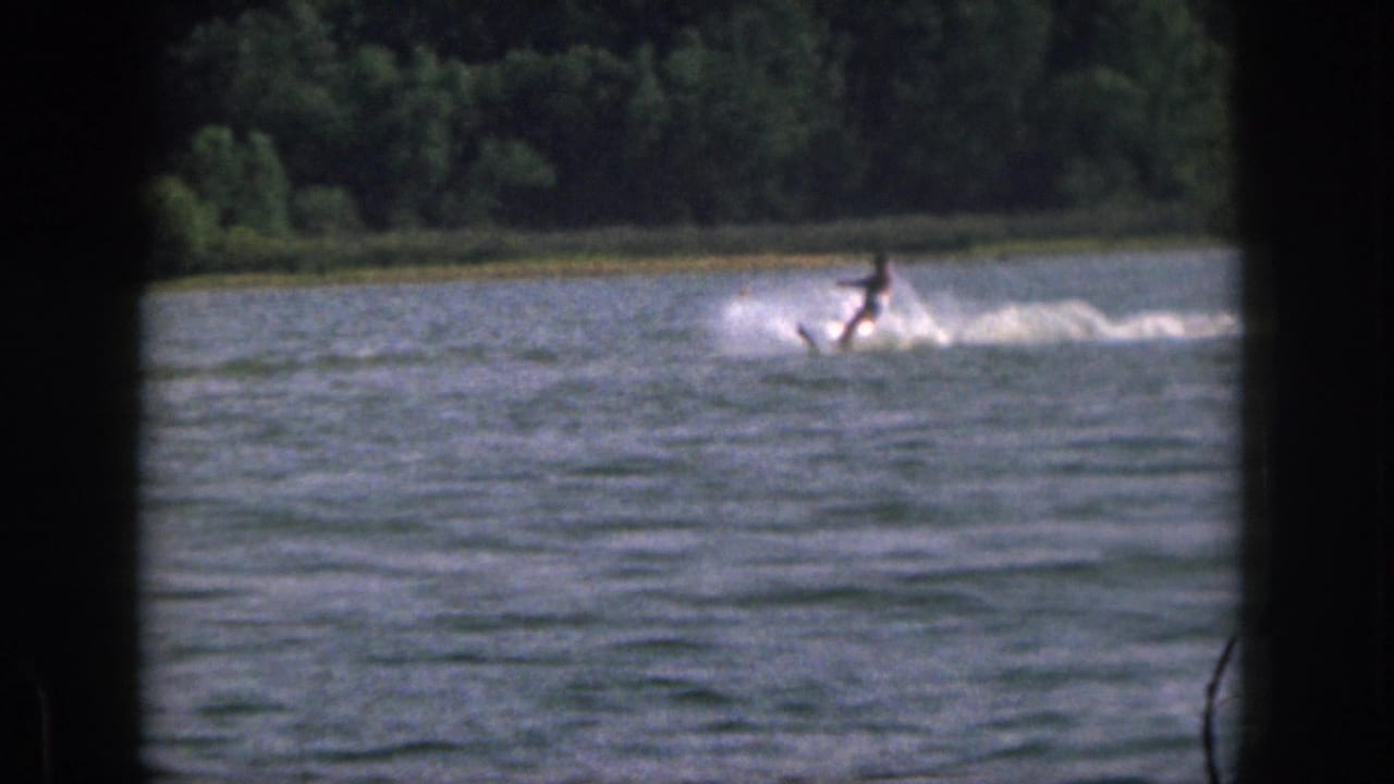 1961 Michigan 8mm footage shows a distant water skier skimming across a lake with trees along the far shore.