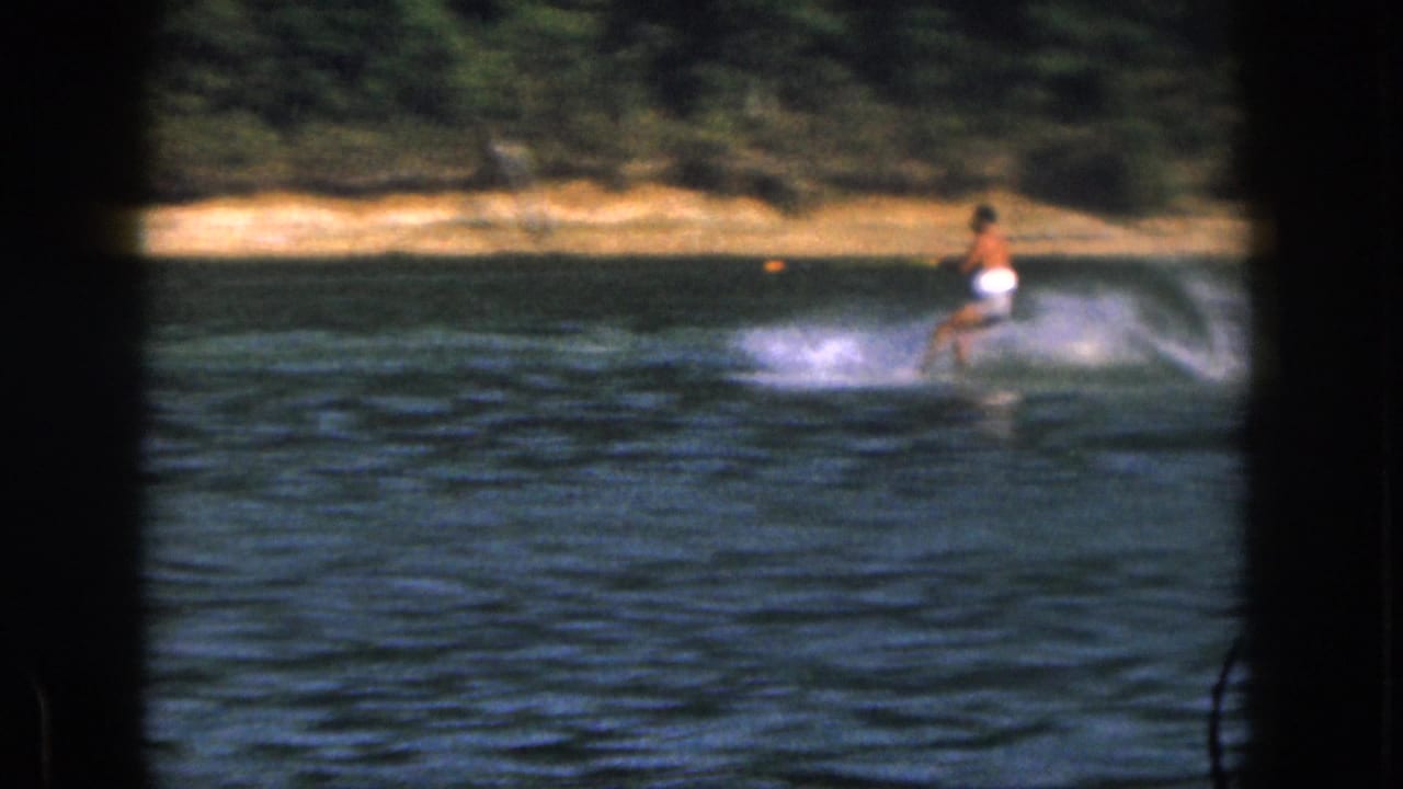 Water skier in white trunks leaning back as spray rises behind him.