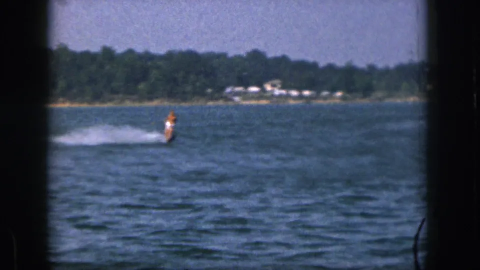 A wider 1961 Michigan lake view shows the skier farther away, with spray, trees, and distant lakeside structures.