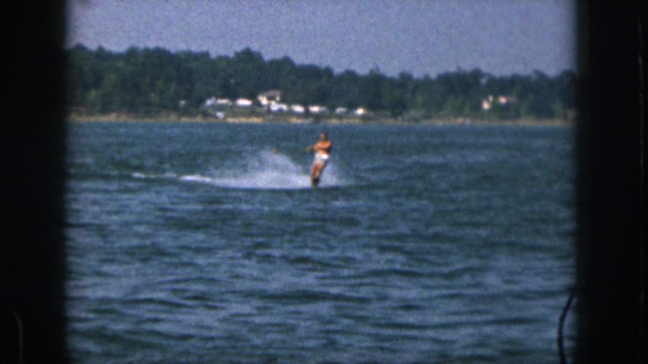 The water skier continues across choppy blue water, framed by dark 8mm gate edges.