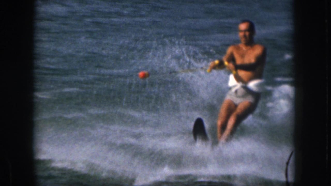 1961 Michigan 8mm frame showing an adult man water skiing on a river, holding a tow rope as white spray rises around him.