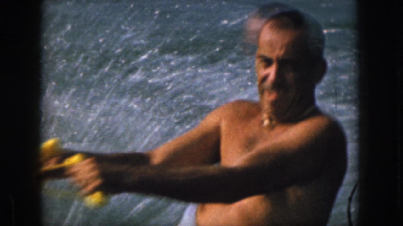 Close 8mm view of the water skier's face and arms as he holds a yellow tow handle against a spray-filled river background.