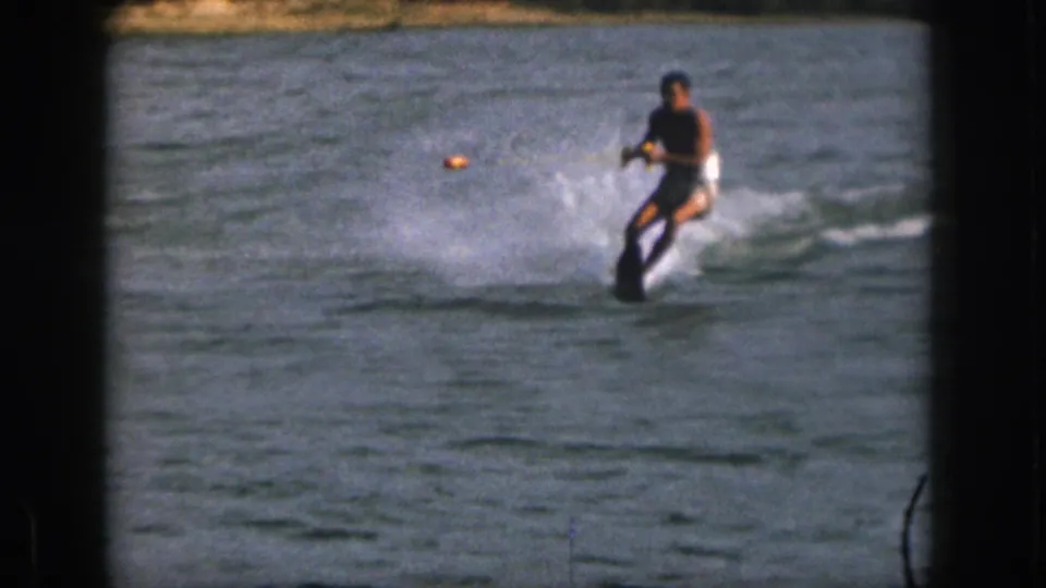 1961 Michigan 8mm frame showing the skier closer to camera, holding the tow handle as spray rises from the skis.