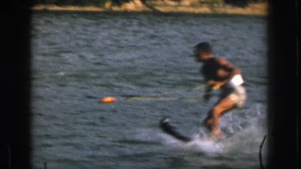 1961 Michigan home-movie frame showing a close, soft-focused water skier leaning forward as the tow rope cuts across the lake.