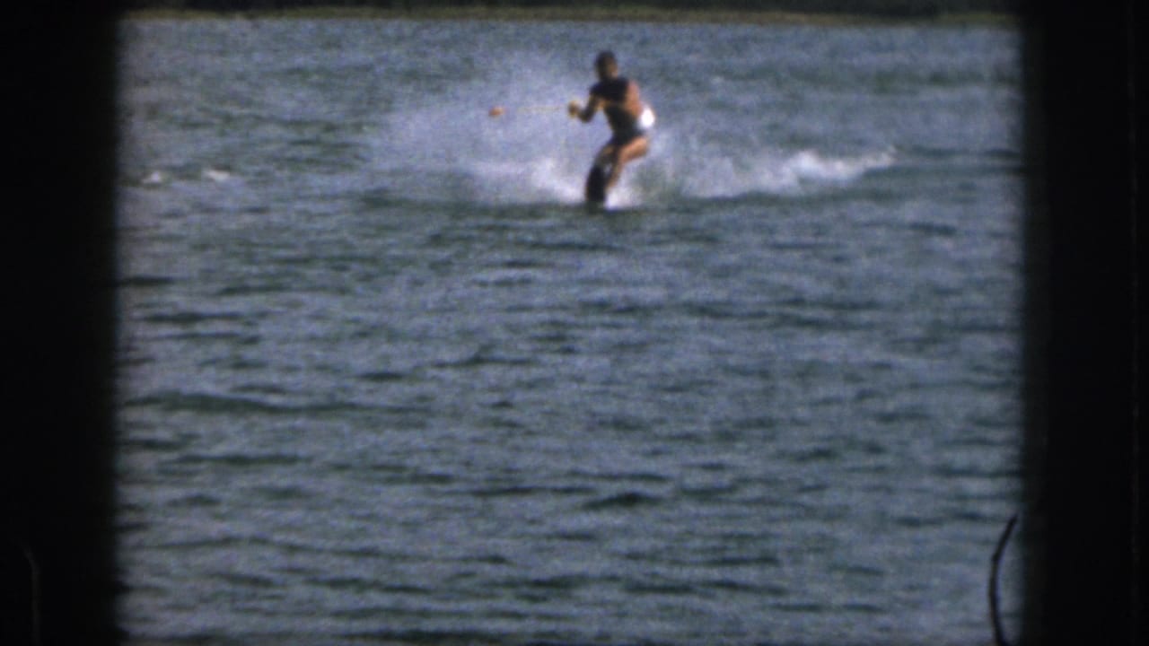 A man water skis across a lake behind a tow rope with distant shoreline beyond the water.