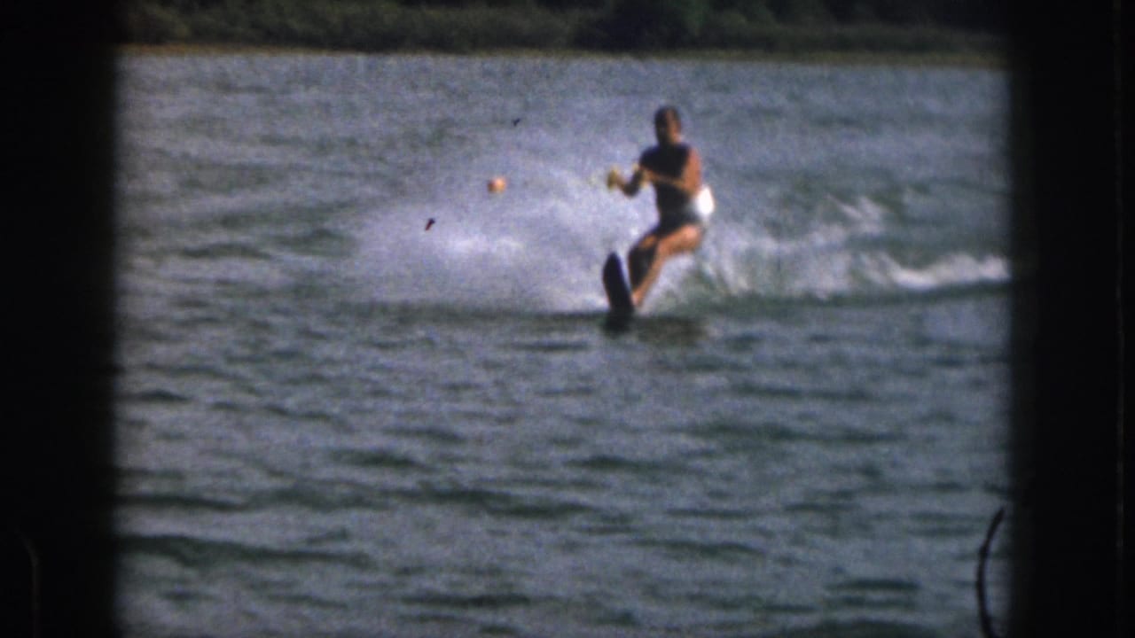 The water skier leans into a turn, pulling a tow rope as spray rises behind him.
