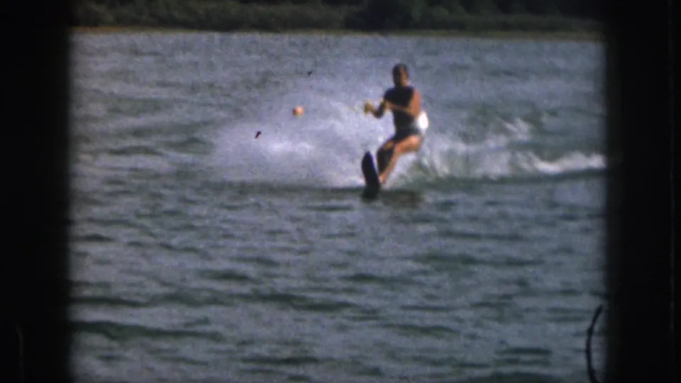 The skier carves across the Michigan lake on a single ski, leaning back against the tow rope as a fan of water spray trails from the turn.
