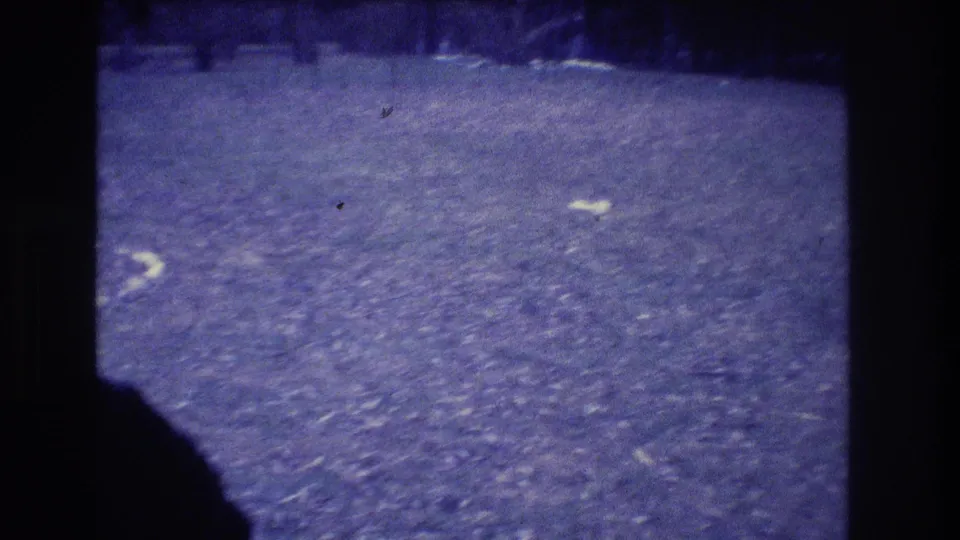 1973 Medford, New Jersey 8mm frame showing an empty grassy field, dark film borders, and a shadowed edge in the foreground.