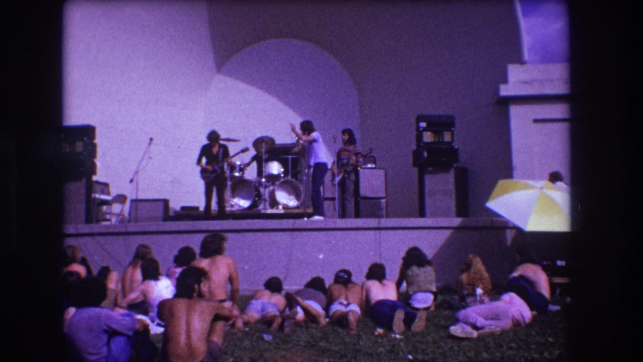 1973 Medford, New Jersey home-movie frame of a rock band on an outdoor stage with young adults seated on the lawn.