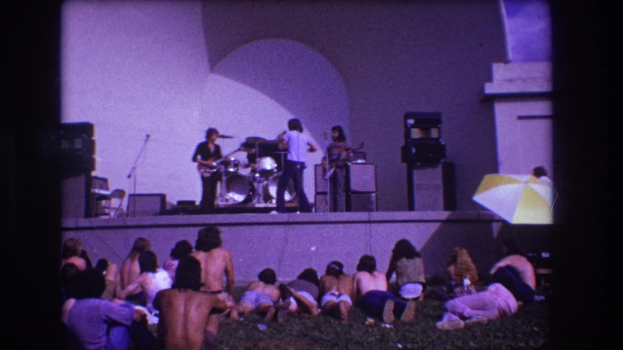 1973 Medford outdoor concert frame showing band members performing above a relaxed lawn audience.