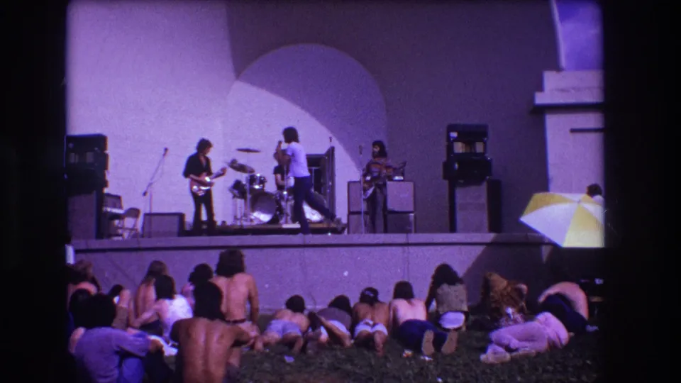 1973 Medford home-movie frame of a small outdoor rock concert with amplifiers, drum kit, and relaxed lawn audience.