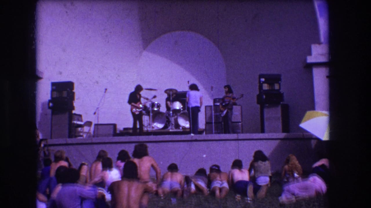1973 Medford, New Jersey 8mm frame showing a rock band performing on a raised stage before a seated grass audience.