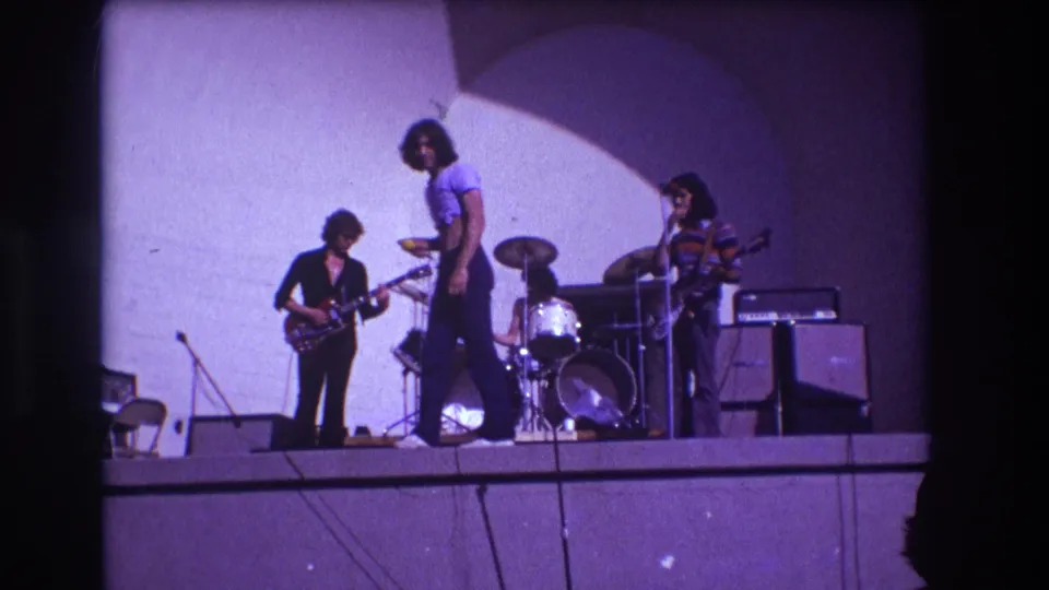 1973 Medford, New Jersey stage frame with a cropped-shirt singer centered between guitar, drums, and bass.