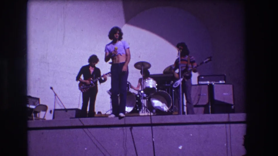 1973 Medford concert frame showing the singer at front with guitarist, drummer, and bassist on the raised stage.