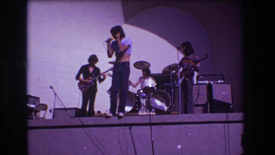 Home-movie frame from the 1973 Medford performance showing the singer closer to the microphone with the band arranged behind him.