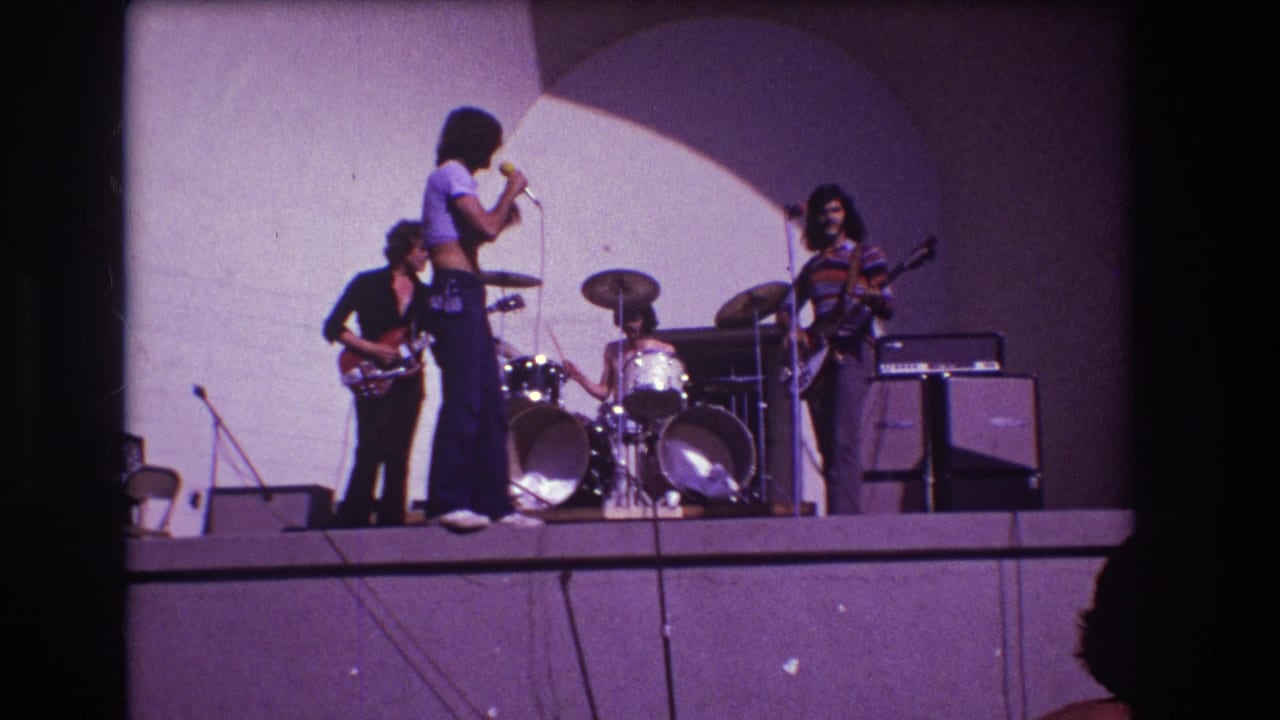 1973 Medford, New Jersey 8mm frame with the singer turned toward the drummer as two guitarists stand near amplifiers on a simple raised stage.