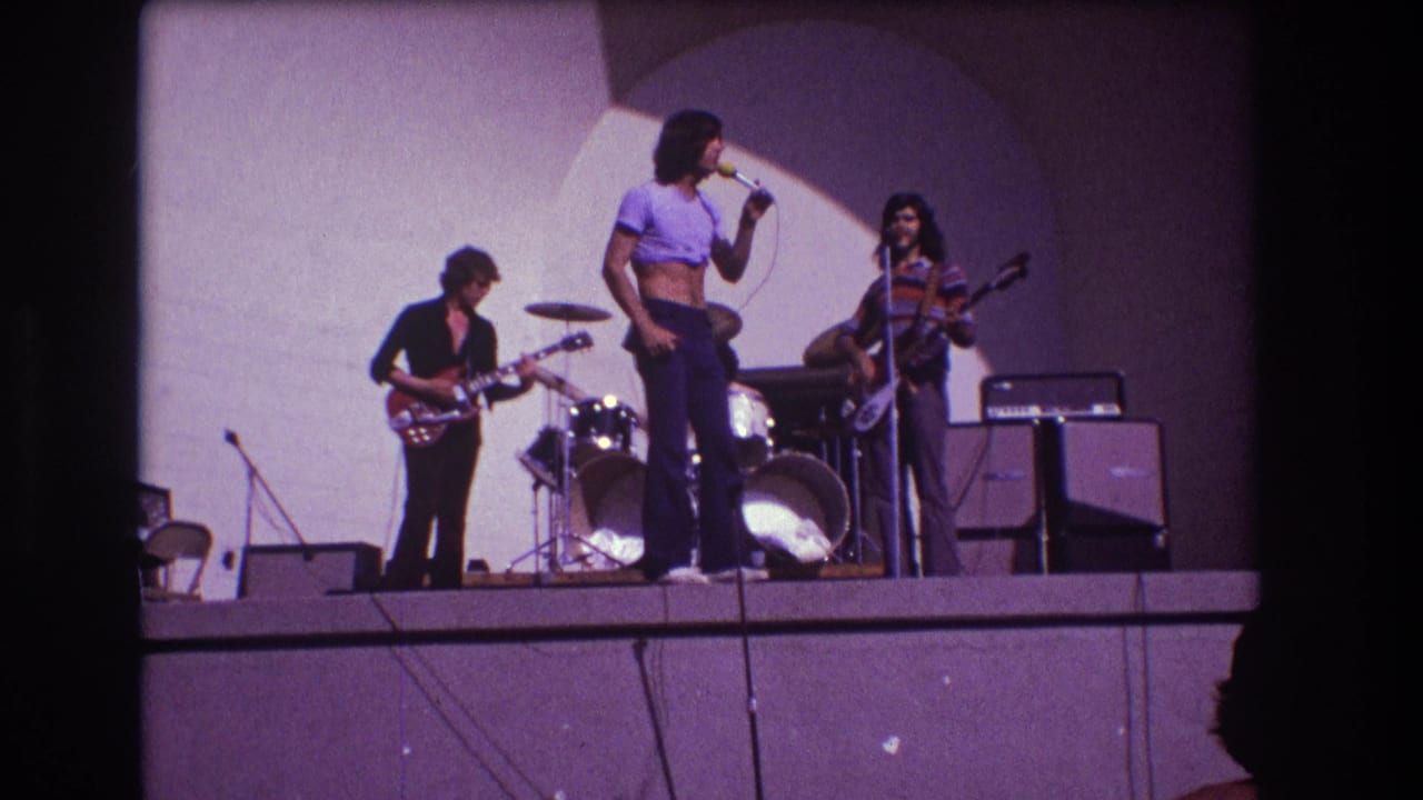 1973 Medford, New Jersey frame with the front man turned toward the band as guitarist, bassist, and drummer continue playing on stage.