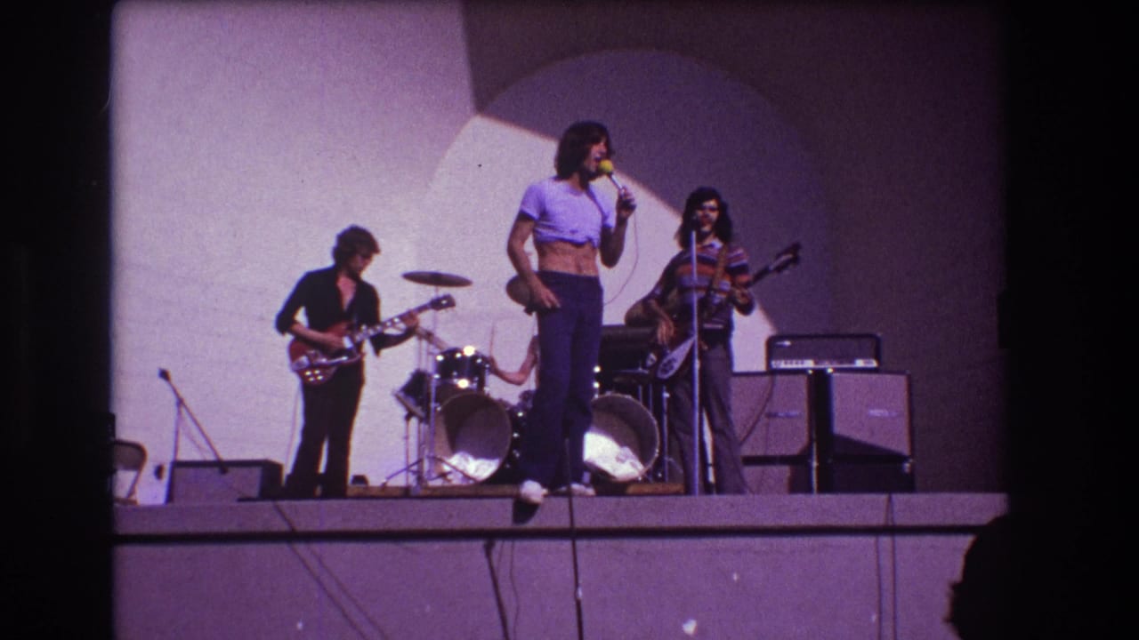1973 Medford, New Jersey frame of the band mid-performance, with the singer holding the microphone while guitar, bass, drums, and stage amplifiers remain visible.