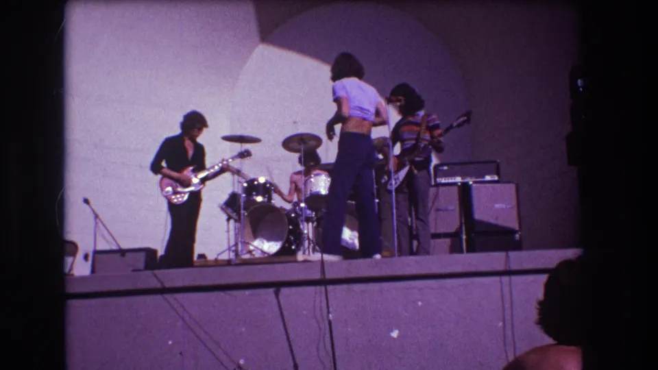 1973 Medford, New Jersey home-movie frame showing the singer turned toward the drummer as the band prepares on stage.