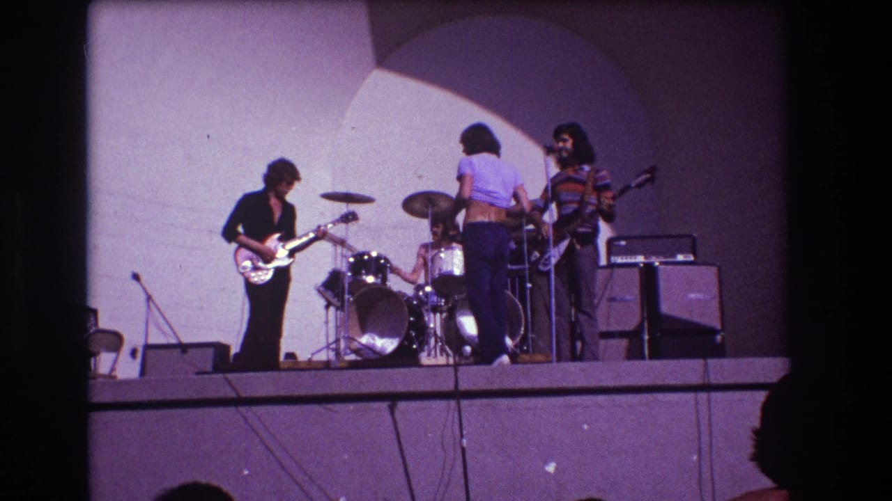 Rock band on a raised stage with guitarist, drummer, singer, and bassist.