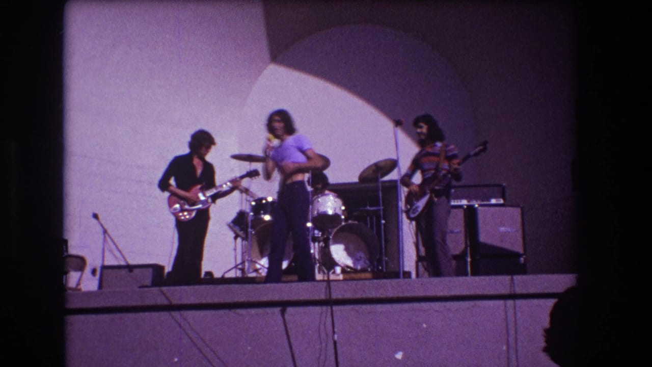 Singer stands near center stage while guitarist, drummer, and bassist play.