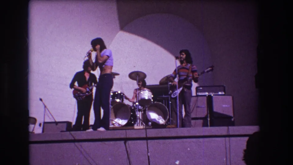 1973 Medford 8mm still of a small rock band, with a vocalist near the front edge of the stage and instruments arranged behind.