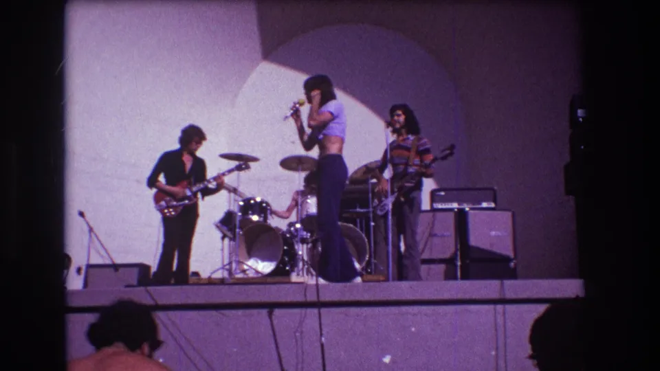 1973 Medford, New Jersey 8mm still showing the singer at the microphone with guitarist, drummer, bassist, stage amps, and audience silhouettes.